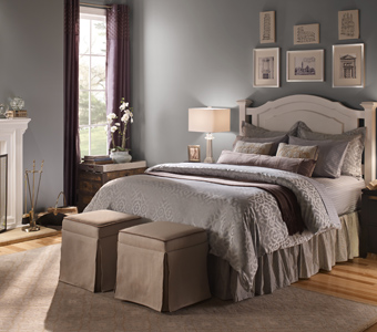 Gray bedroom with framed pictures, white fireplace, and gray bed.
